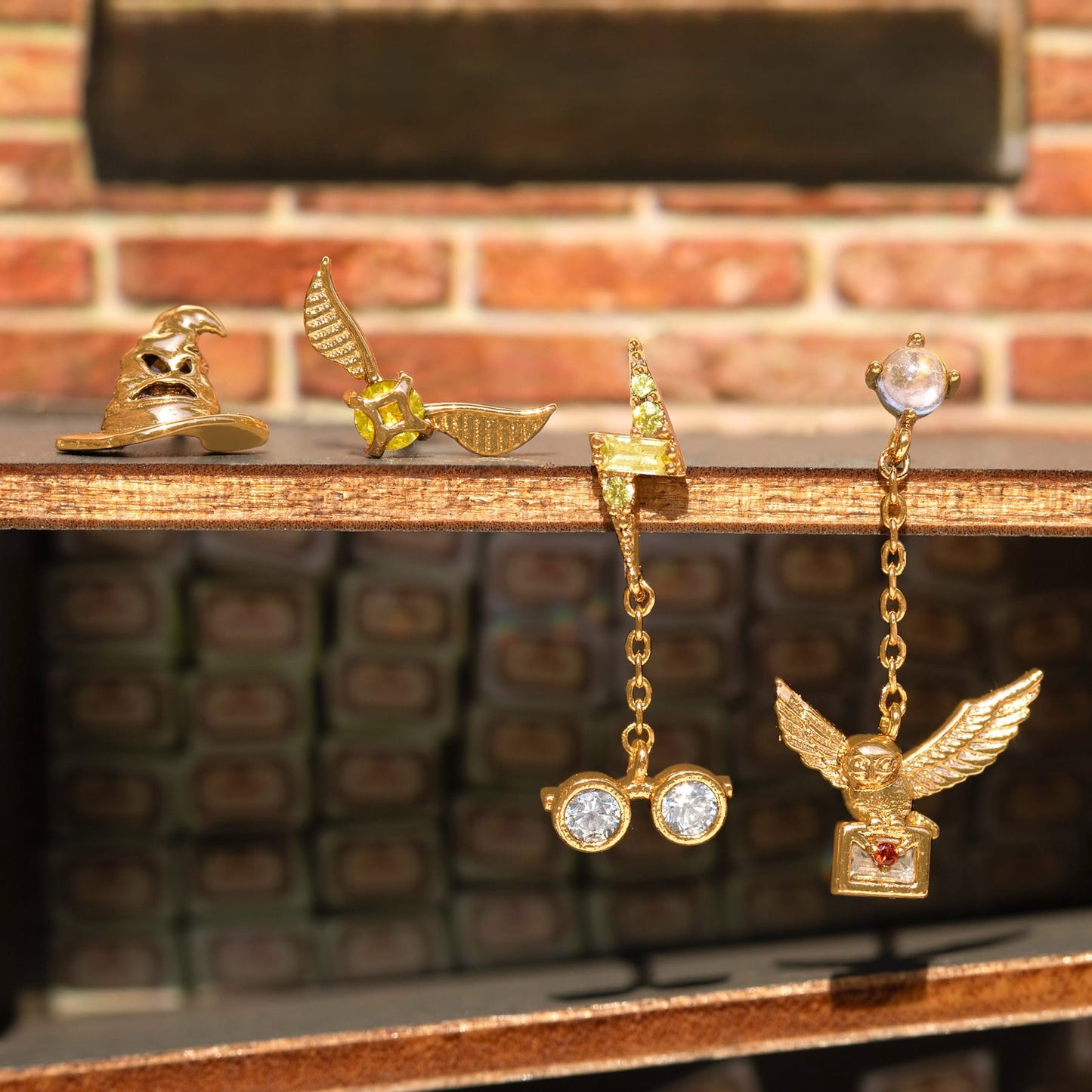 Gold Harry Potter earrings on a wooden surface with a brick wall background