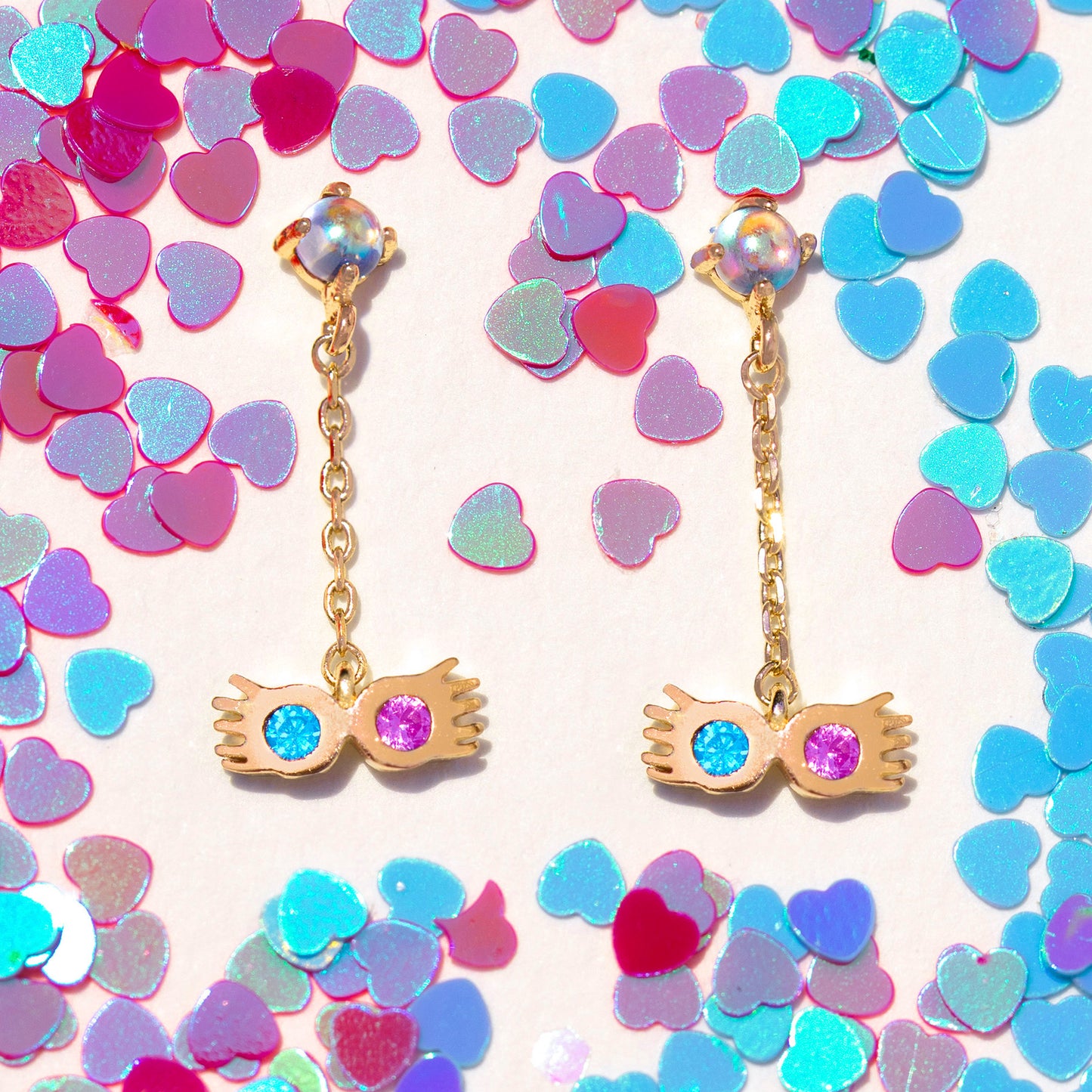 Gold earrings with colorful gemstones on a heart-shaped confetti background