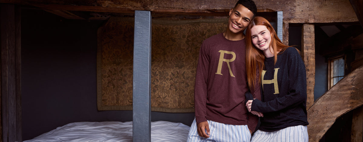 Two young people sit in a dorm room at Hogwarts wearing matching H and R pyjama sets.