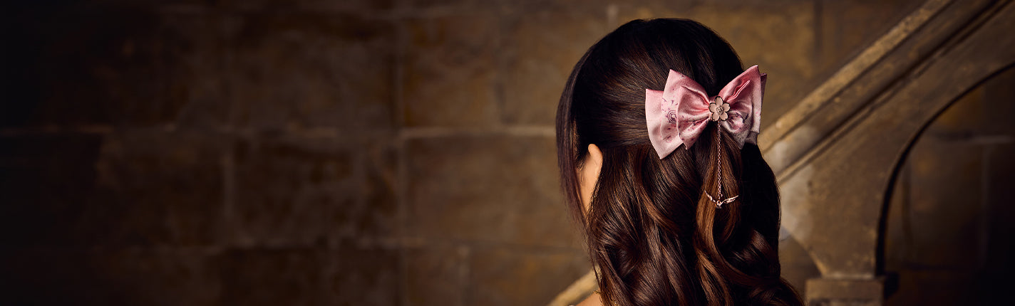 Person with a pink bow in their hair standing against a stone wall.