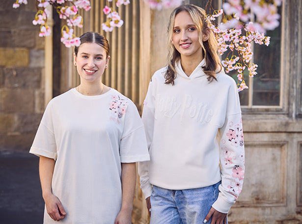 Two women wearing white Harry Potter apparel with floral designs standing in front of a building with cherry blossoms.
