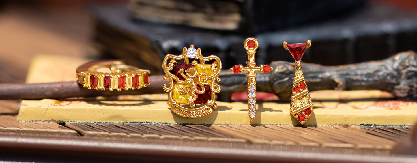 Gold and red Gryffindor jewelry pieces on a wooden surface with a blurred background