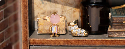 Decorative earrings including a gold sock and pink gemstone Dobby on a shelf.