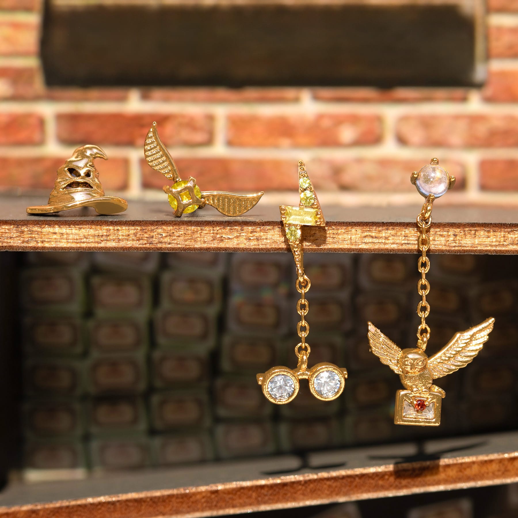 Gold Harry Potter earrings on a wooden surface with a brick wall background