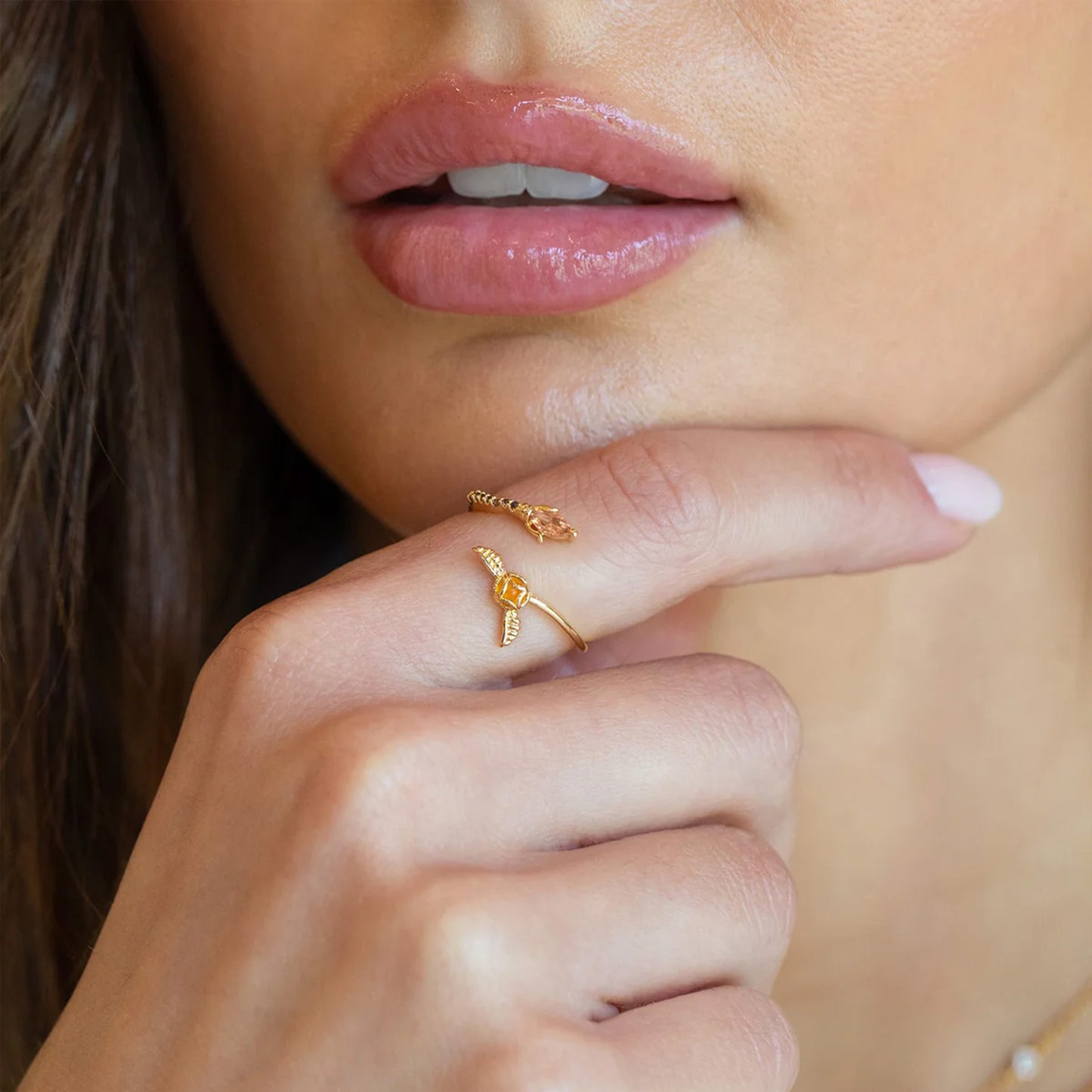 Close-up of a woman's hand with a gold ring on her finger, wearing pink lipstick.