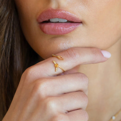Close-up of a woman's hand with a gold ring on her finger, wearing pink lipstick.