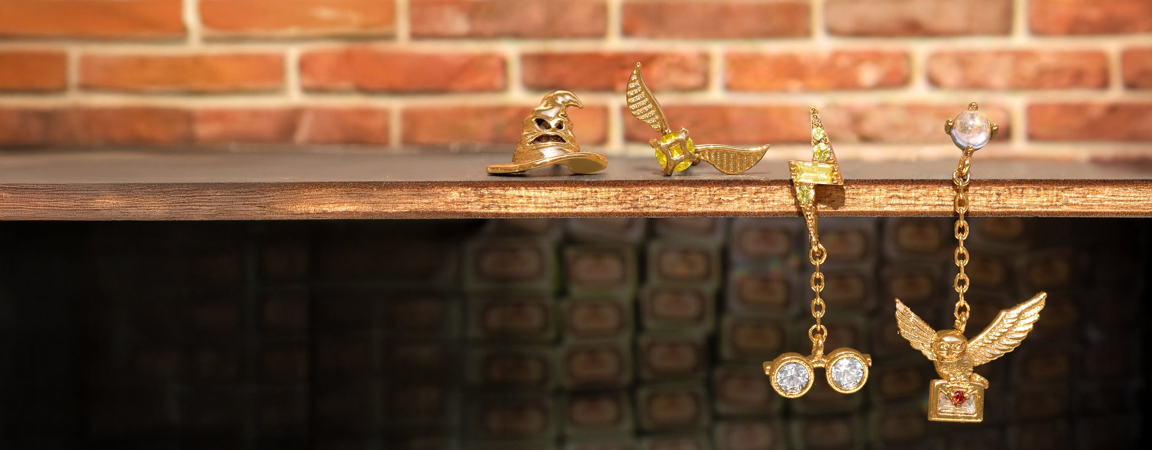Gold earrings with intricate designs on a wooden surface against a brick wall background