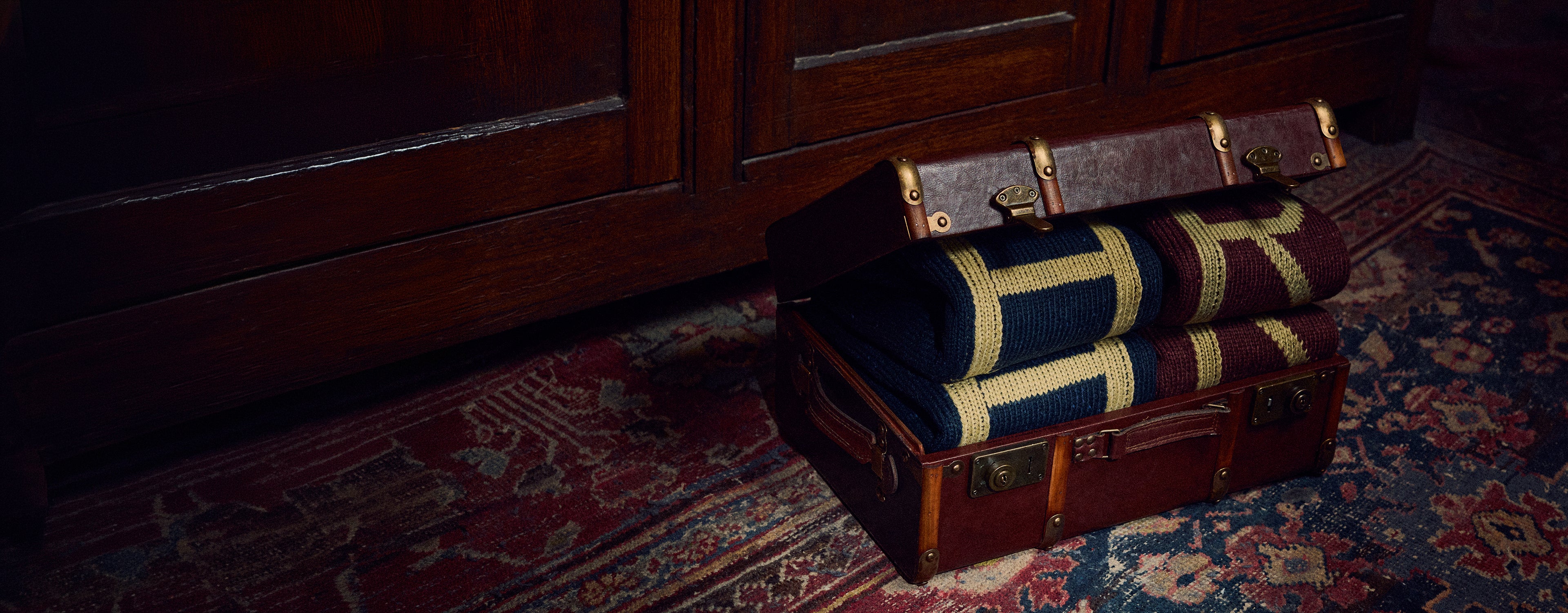 Vintage suitcase with rolled-up H and R Jumpers on a patterned rug