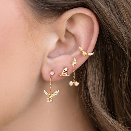 Close-up of an ear with gold earrings featuring the golden snitch and small gemstones.