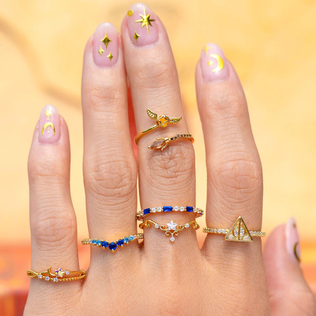 Hand wearing multiple gold rings with various designs on a blurred background
