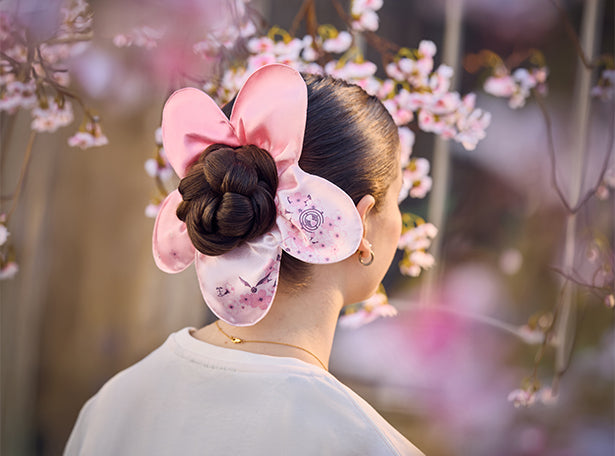 Person with a traditional hairstyle featuring sakura pink floral hair accessories against a cherry blossom background