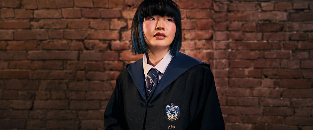 Person wearing a dark blue Ravenclaw school uniform with a tie against a brick wall.